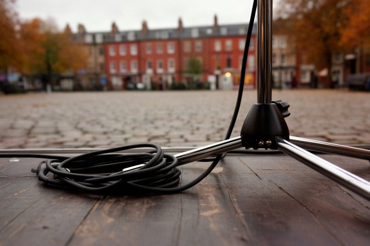 Zwinięty kabel i statyw mikrofonowy na drewnianej scenie plenerowej na brukowanym placu małego miasta