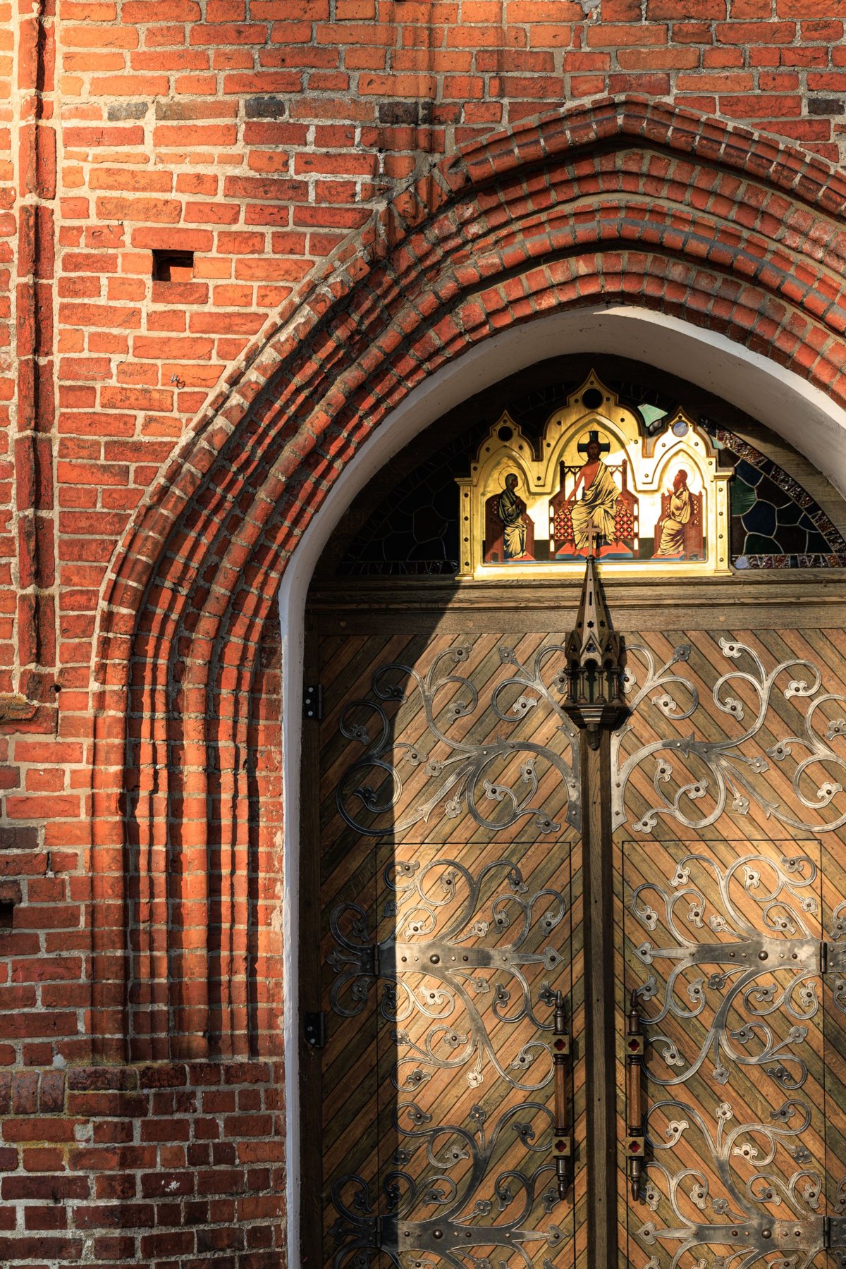 Ostrołukowy portal z czerwonej cegły gotyckiej w popołudniowym świetle